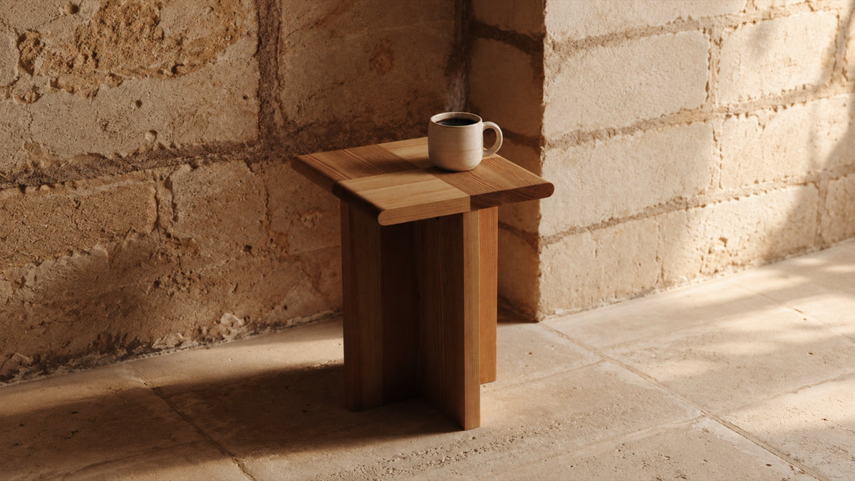 A mug of coffee on a wooden stool against a stone wall